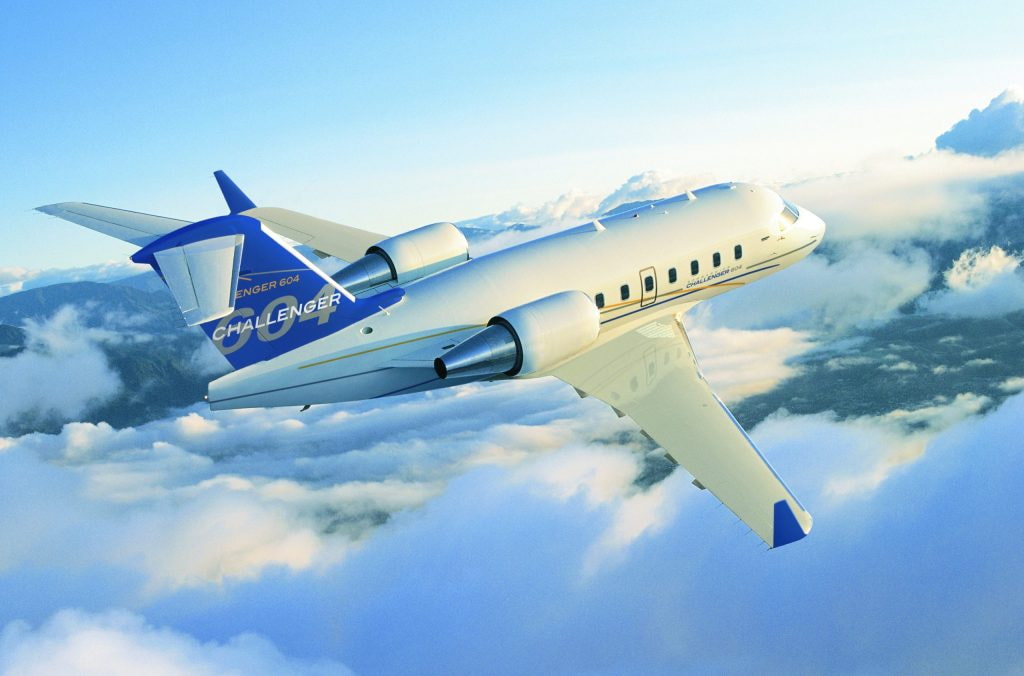 Challenger 604 flying above the clouds with mountain scenery in the background