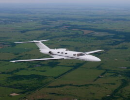 Citation Mustang flying over green countryside with a clear sky.