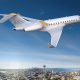 Bombardier Global 5000 flying over a cityscape with the Space Needle visible, set against a clear blue sky.