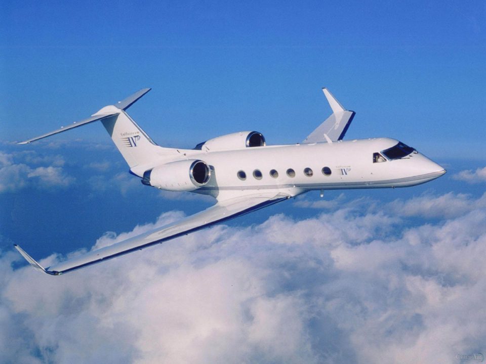 Gulfstream IV-SP business jet in flight above the clouds on a clear blue day.