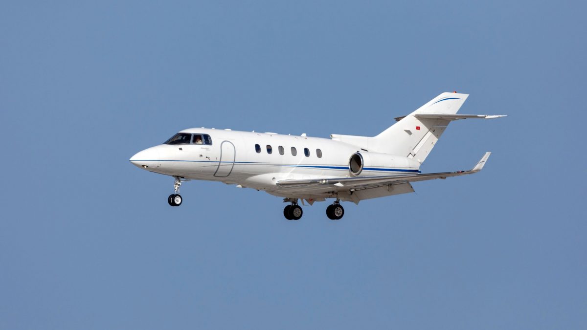 Mid-size white Hawker 900XP private jet in flight against a clear blue sky