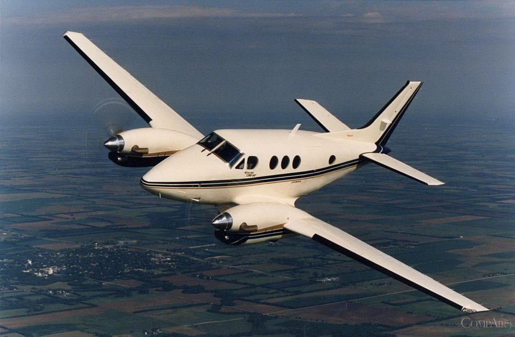 King Air C90SE twin-turboprop aircraft in flight with beige and navy stripe livery