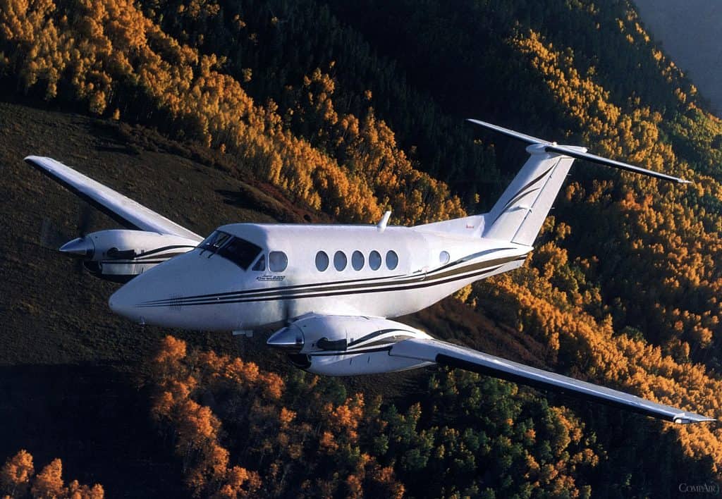 King Air 350 twin turboprop aircraft flying over a forested mountain in autumn