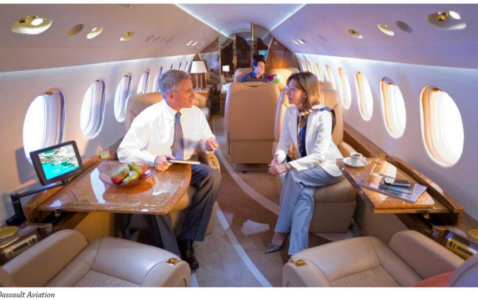 Corporate professionals seated inside a Dassault private jet cabin with luxurious furnishings and natural lighting.