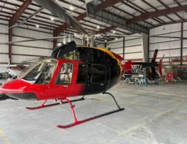1999 Bell 407 helicopter in red and black paint parked in hangar with SkyNews decals removed