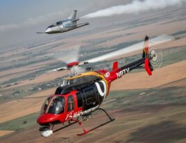 1999 Bell 407 helicopter in flight with light jet trailing over farmland