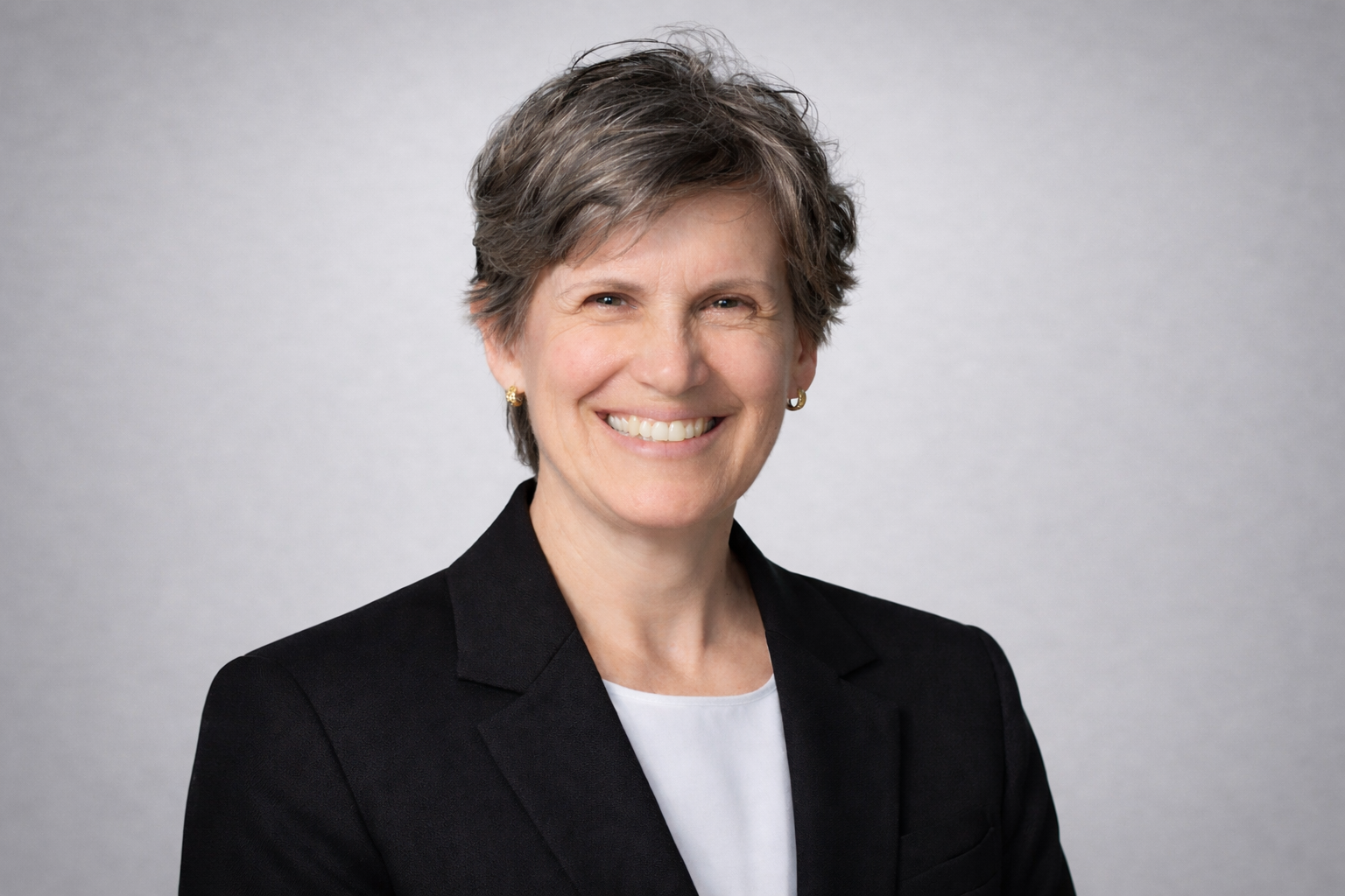 Professional headshot of a business executive smiling, wearing a black blazer against a neutral background